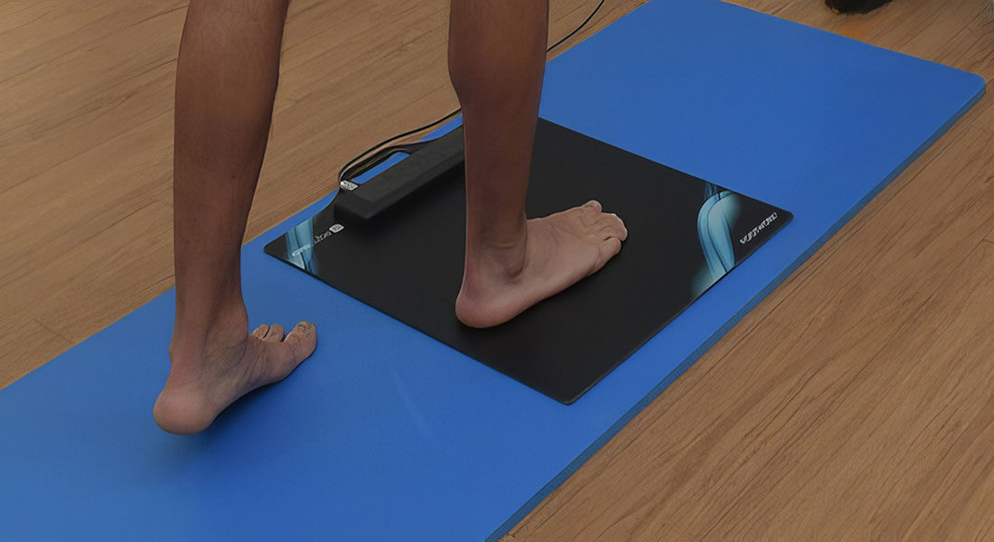 Άτομο στέκεται σε πλατφόρμα ανάλυσης πελματικών πιέσεων για αξιολόγηση βάδισης και στάσης. Η συσκευή μετρά τα σημεία πίεσης στα πέλματα των ποδιών.