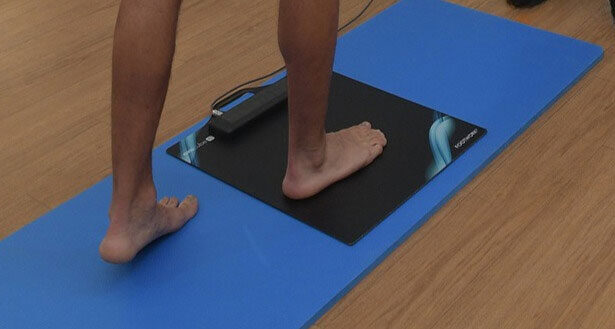 Άτομο στέκεται σε πλατφόρμα ανάλυσης πελματικών πιέσεων για αξιολόγηση βάδισης και στάσης. Η συσκευή μετρά τα σημεία πίεσης στα πέλματα των ποδιών.