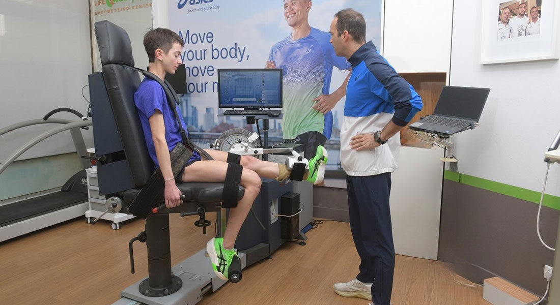 Νεαρή αθλήτρια σε ισοκινητικό δυναμόμετρο για αξιολόγηση γονάτου με επαγγελματία φυσιοθεραπευτή. Το μηχάνημα μετρά τη δύναμη σε οθόνη υπολογιστή.