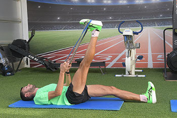 Ο αθλητής βρίσκεται σε ύπτια θέση σε γαλάζιο στρώμα άσκησης με τα πόδια ασφαλισμένα στη συσκευή και εκτελεί ισομετρική άσκηση οπίσθιων μηριαίων.