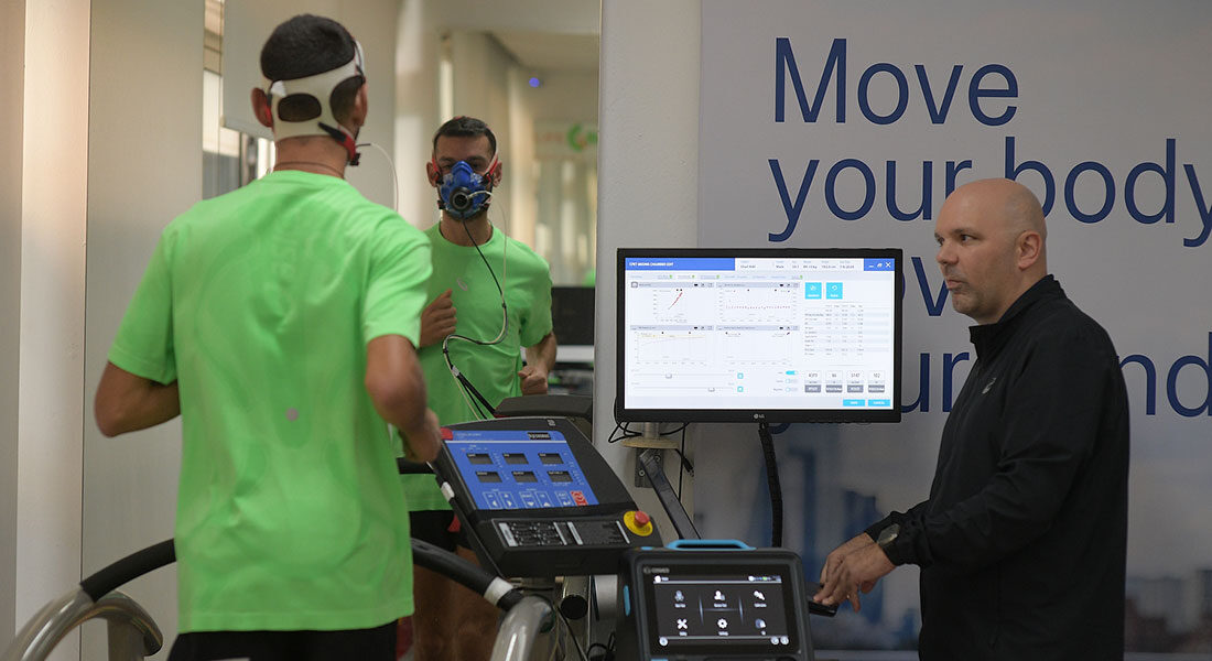 Επαγγελματίας εργοφυσιολόγος παρακολουθεί αθλητή κατά τη διάρκεια εξέτασης VO₂ max πάνω σε διάδρομο τρεξίματος.