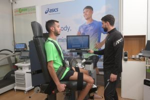 Ισοκινητική αξιολόγηση κάτω άκρου σε ειδικό δυναμόμετρο. Το πόδι του αθλητή είναι ασφαλισμένο στη συσκευή που φοράει πράσινο αθλητικό παπούτσι Asics. Η μηχανή μετρά τη δύναμη, την κινητικότητα και τη σταθερότητα του αστραγάλου με γωνιόμετρο που δείχνει μοίρες κίνησης. Χρησιμοποιείται για αποκατάσταση τραυματισμών, πρόληψη και αξιολόγηση μυοσκελετικής απόδοσης.