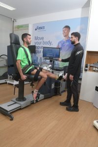 Ισοκινητική αξιολόγηση κάτω άκρου σε ειδικό δυναμόμετρο. Το πόδι του αθλητή είναι ασφαλισμένο στη συσκευή που φοράει πράσινο αθλητικό παπούτσι Asics. Η μηχανή μετρά τη δύναμη, την κινητικότητα και τη σταθερότητα του αστραγάλου με γωνιόμετρο που δείχνει μοίρες κίνησης. Χρησιμοποιείται για αποκατάσταση τραυματισμών, πρόληψη και αξιολόγηση μυοσκελετικής απόδοσης.